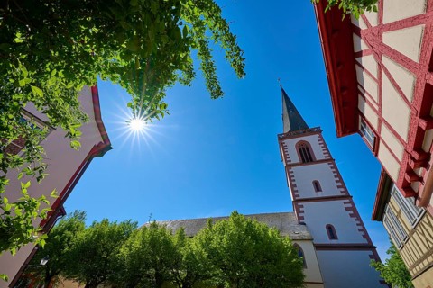 View of a church tower with half-timbered houses and sun through trees, St Michael parish church,