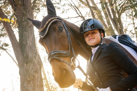 Young equestrian in classical dressage attire stands confidently beside her horse Sunlight filters
