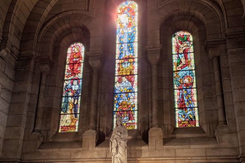 Three colourful windows with a statue in front of them, sunlight streaming through the middle