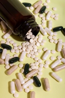 An open glass bottle spills assorted pills and capsules onto a light green surface. The variety of