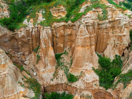 Close-up of erosion rocks with green vegetation in a hilly landscape, aerial view, Râpa Ro?ie, Rapa