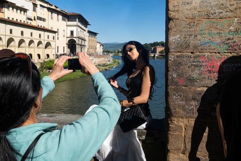 Tourist takes pictures of a young woman wearing sunglasses on Ponte Vecchio, Arno, old town,