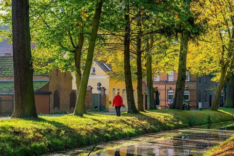 Woman in red jacket walking through a park with autumn coloured trees at the river Nieplitz, behind