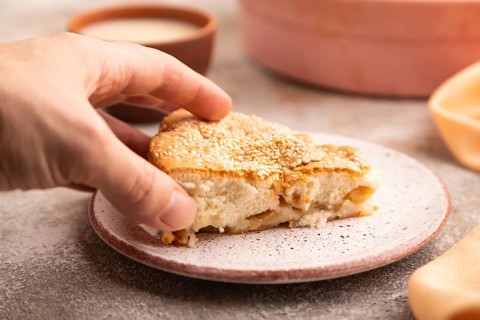 Apple Charlotte cake with hand on brown concrete background and orange linen textile, cup of milk,