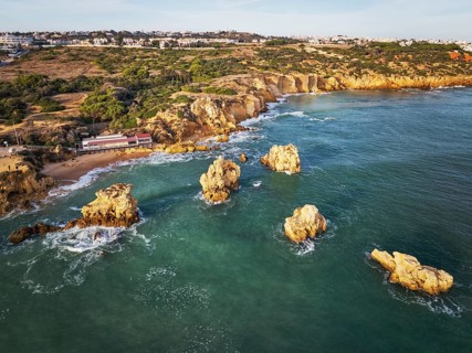 Aerial view of Praia dos Arrifes shoreline with sea stacks, cliff paths, beach access and waves