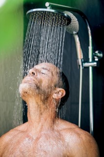 A man stands under a shower with closed eyes, enjoying the refreshing sensation of water cascading