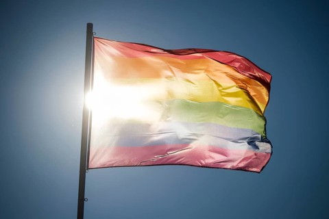 Traditional pride flag and rainbow flag form a silhouette in backlight with sun glare in the