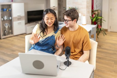 Multiethnic young couple waving at their followers while recording a podcast or live streaming from