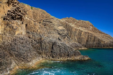 Steep cliffs with unique basalt columns on the edge of a calm ocean, Glaronisia, Glaronesia, Milos,