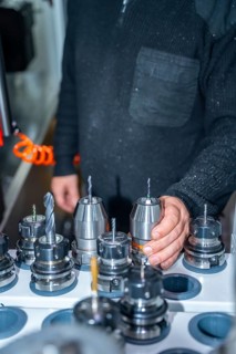 Vertical photo of an unrecognizable worker holding one lathe among a collection of lathes in a cnc