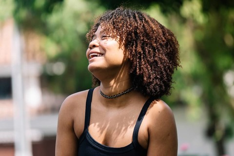 A young black woman smiles brightly while sitting outdoors in a Bogota park Her carefree