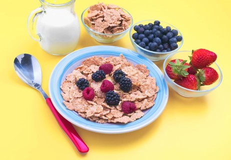 A vibrant breakfast spread with cereal, fresh berries, strawberries, and milk on a yellow