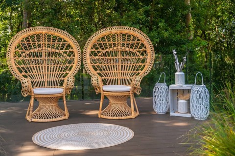 Two wicker peacock chairs and white decorations stand on a wooden deck, creating a bohemian