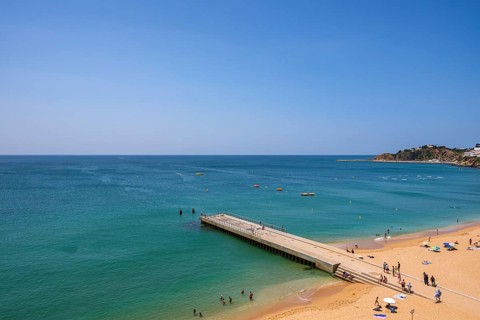 A sunny beach with crystal clear water, a jetty and people relaxing on the beach, Albufeira, Faro,