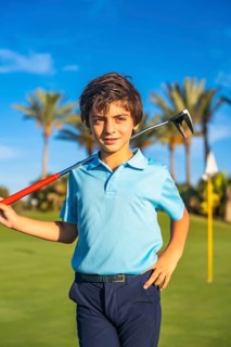 Vertical close-up portrait of a caucasian chic boy posing with gold club on shoulder on a course