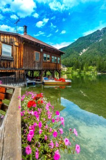 Pedal boats moored beneath a charming wooden house adorned with colorful flowers at lake dobbiaco