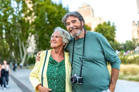Happy elder woman embraced to man with photographic camera in a park