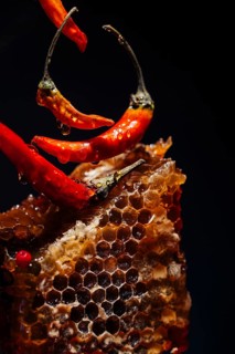 Close up of vibrant red chilies and a honeycomb against a dark background. Droplets add texture and