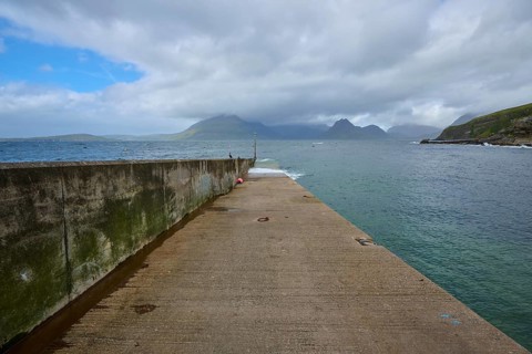 Long pier stretches out to sea with views of distant mountains and clouds in the sky, Elgol Beach,