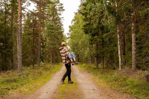 A man carries a woman in his arms while walking along a peaceful forest path. Surrounded by lush