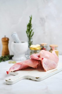 A hind legs of rabbit meat on a cutting board ready for preparation. Various kitchen tools, spice