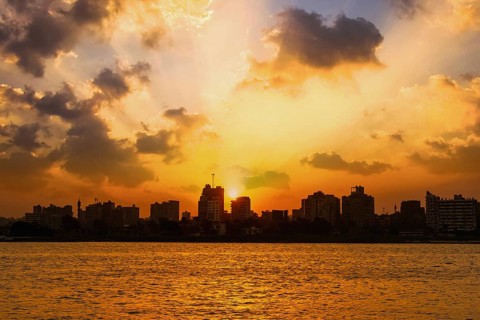 Orange sunset on the Nile river, the sun hides in the buildings of the city of Cairo in the