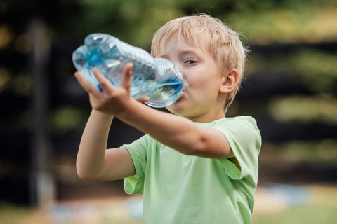 Six yeras old boy drinking water in the garden