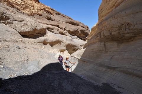 Two hikers in a rocky gorge crisscrossed by sun and shade, Death Valley National Park, Mojave
