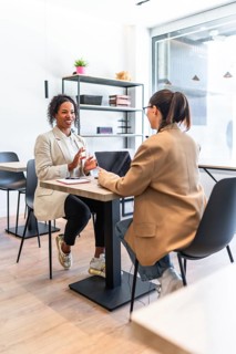 Two businesswomen are having a productive meeting, discussing a project over a laptop in a bright,