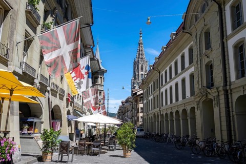 Münstergasse with historic houses decorated with flags, tower of the Bernese Minster in the back,