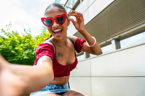 Young woman with heart shaped sunglasses and a wide smile enjoying a moment of self expression and