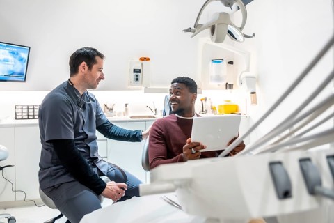 Dentist explaining diagnosis to patient using tablet in modern dental clinic, showcasing technology