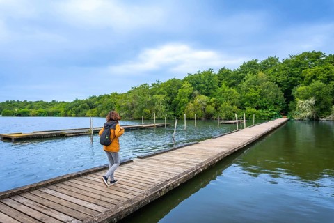 Woman with backpack walking along a wooden pier on lake azur in landes, france, enjoying a peaceful