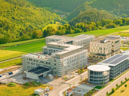 Aerial view of a complex with modern buildings surrounded by green hilly landscape, construction of