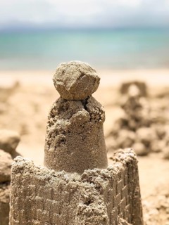 A detailed sand castle stands proudly on the seaside, with intricate designs and a smooth dome,