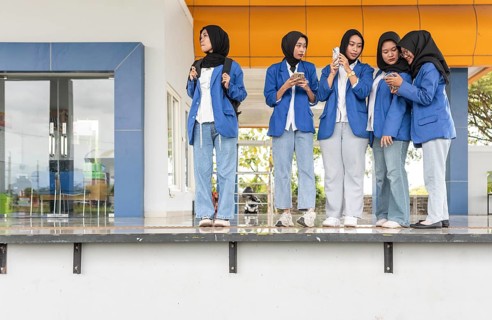 Asian Muslim students in hijabs and blue blazers gather at an educational institution, engaging in