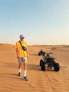 A happy smiling man in a yellow shirt and cap walks near an all terrain vehicle in the expansive