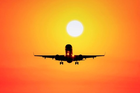 Airplane flying towards sunset in orange sky