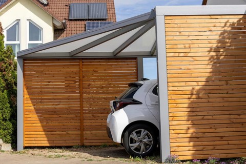 Beautiful carport made of wood and metal with side slatted walls and a fixed roof next to a