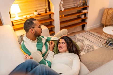 Young couple enjoying a cozy moment on the living room sofa, with the woman resting on the man's
