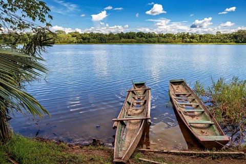 Two wooden boats on the shore of a calm lake with a wooded background and clear blue sky, The Beni