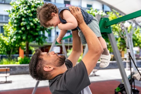 Father lifting up his young son, creating a joyful moment of play and bonding in an urban park