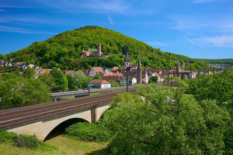 A town with a railway line and bridge, surrounded by green hills and forests, Gemünden am Main,