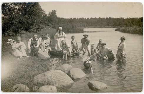 A group of people wearing traditional clothes enjoy a day at the river, accompanied by a dog.