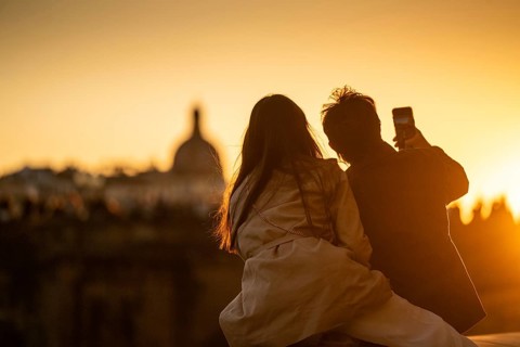 Young couple taking selfie at sunset, back light, urban landscape with dome in background,