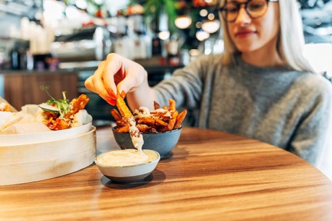 Young woman enjoying sweet potato fries with dip in a trendy urban cafe