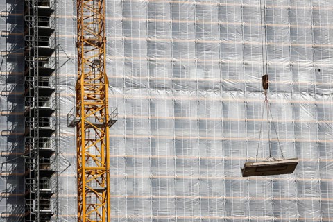 Essen, North Rhine-Westphalia, Germany - Construction crane lifts concrete section in front of