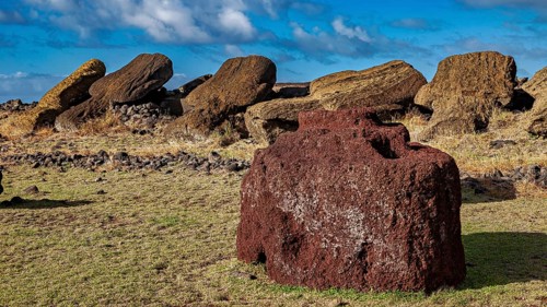 Large reddish stone in front of fallen Moai statues and a cloudy sky, The Moai Statues on Easter