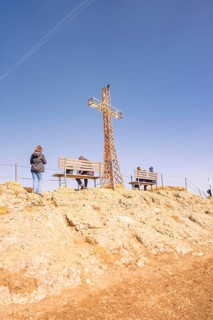 People sitting on benches under a summit cross with a clear view, Hochgrat Mountains, Allgäu Alps,