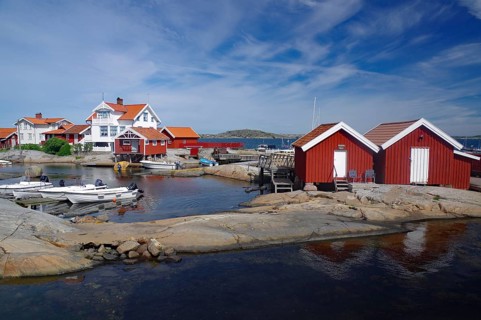 Red wooden houses on rocky coast, boats in calm water, picture under a cloudy sky, archipelago,